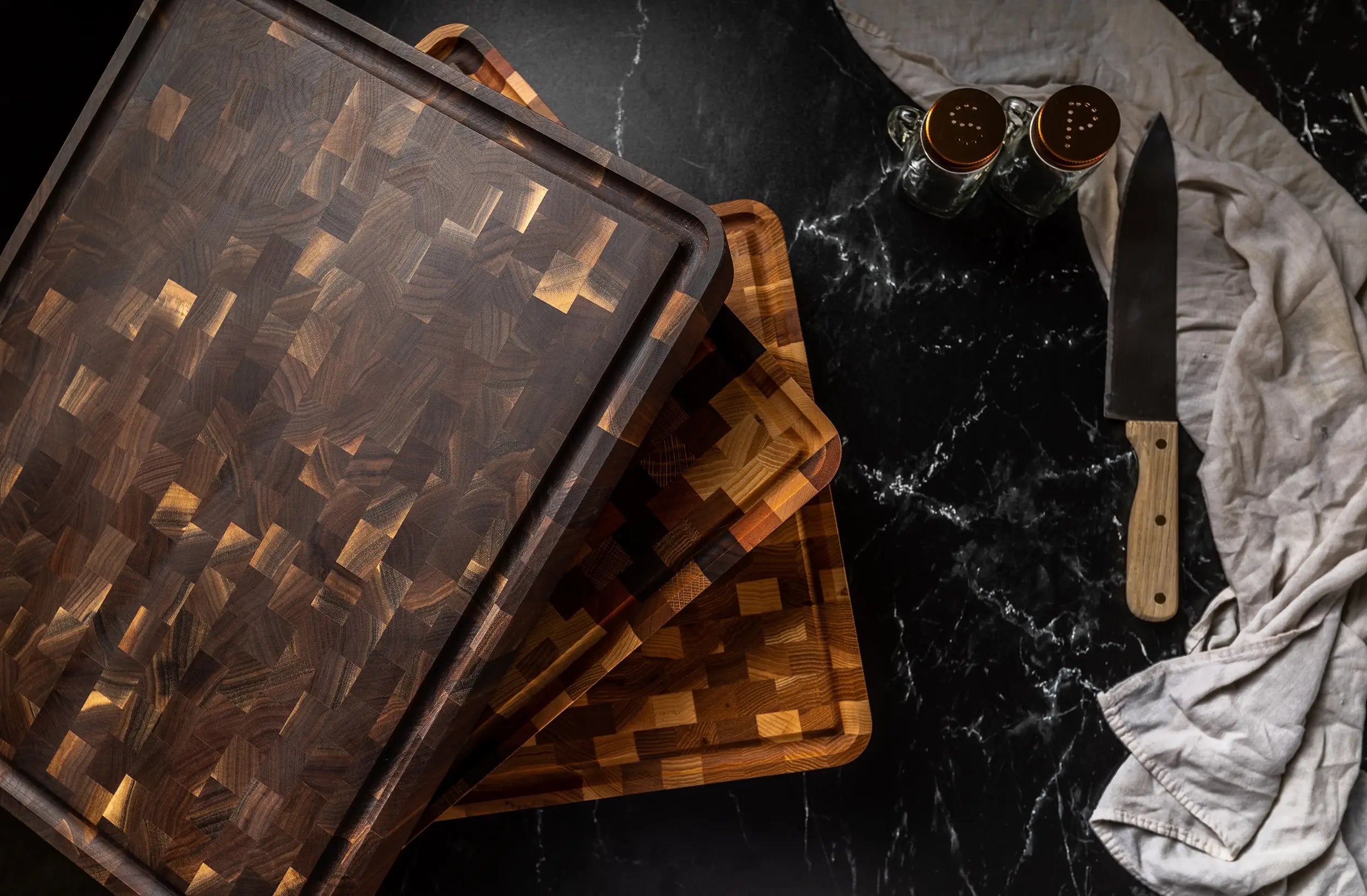 Stack of wooden butcher blocks on a black marble countertop with a knife and spice jars nearby.