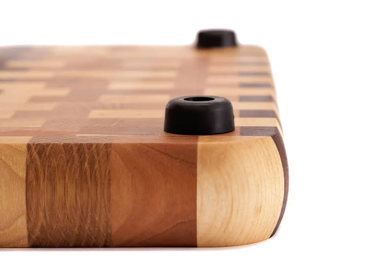 A side view of an end-grain cutting board with a checkered pattern and a black rubber foot, shown against a white background
