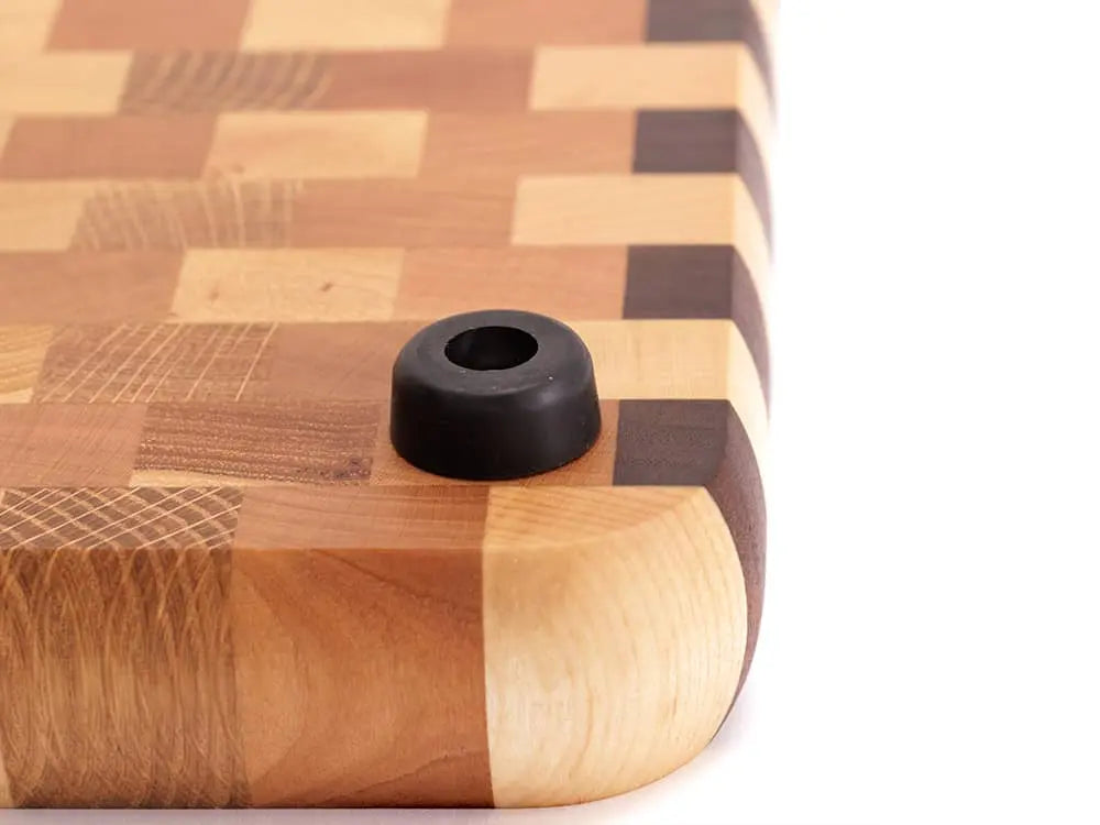 Close-up of an end-grain cutting board corner with a checkered pattern and a black rubber foot, against a white background