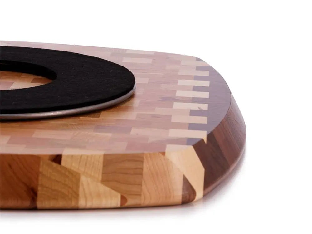 Close-up view of the underside edge of a rectangular end-grain lazy susan with rounded corners, featuring a geometric mosaic pattern in various shades of light and dark brown wood, showing a black protective felt pad, on a white background
