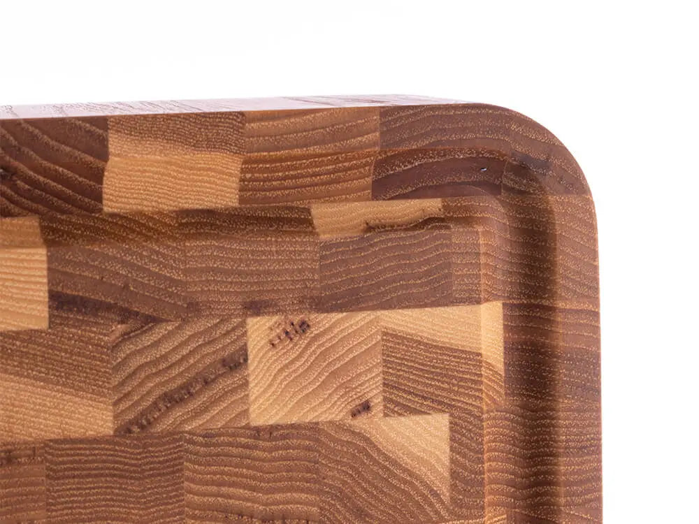 Close-up of a hickory nut end grain butcher block corner with a checkered pattern and a juice groove, against a white background