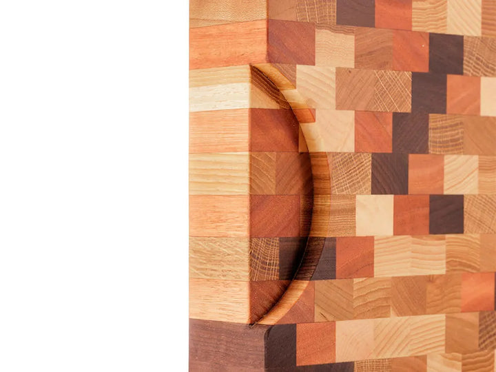 Close-up of an end grain butcher block with a checkered pattern, showing a handle cutout, against a white background