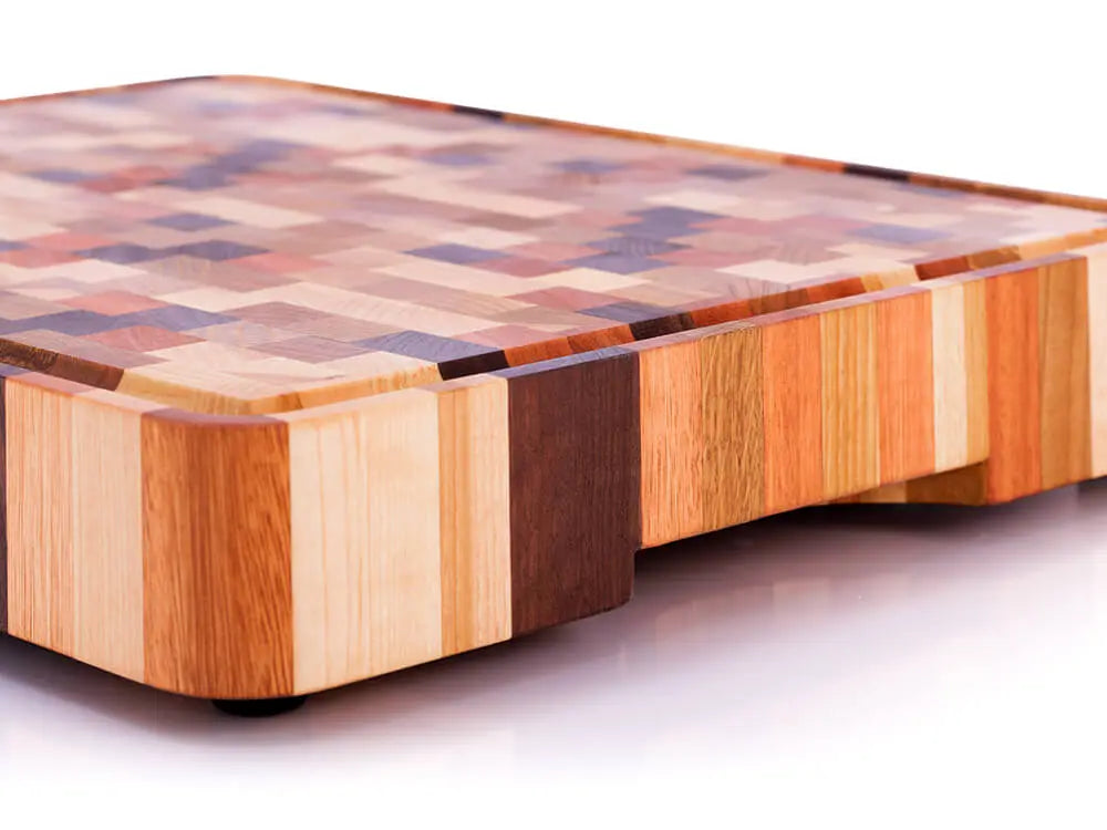 Angled side view of an end grain butcher block with a checkered pattern, handle cutout, and juice groove, against a white background