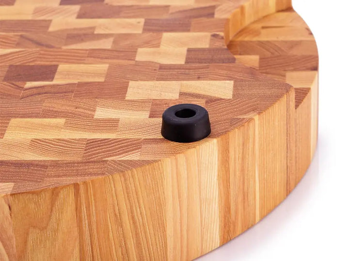 Close-up of a round hickory end grain butcher block with a rubber foot and prominent wood grain pattern.
