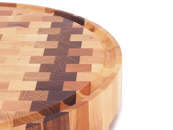 Close-up of a round end grain butcher block with a checkered pattern and juice groove, against a white background