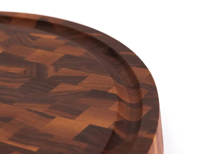 A close-up, top view of a round black walnut end grain cutting board with a checkered pattern, with a focus on its unique juice groove