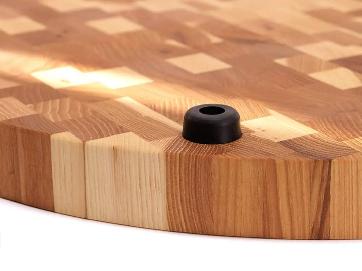 Close-up view of the bottom of a round end-grain cutting board with a checkered pattern and black rubber feet, against a white background