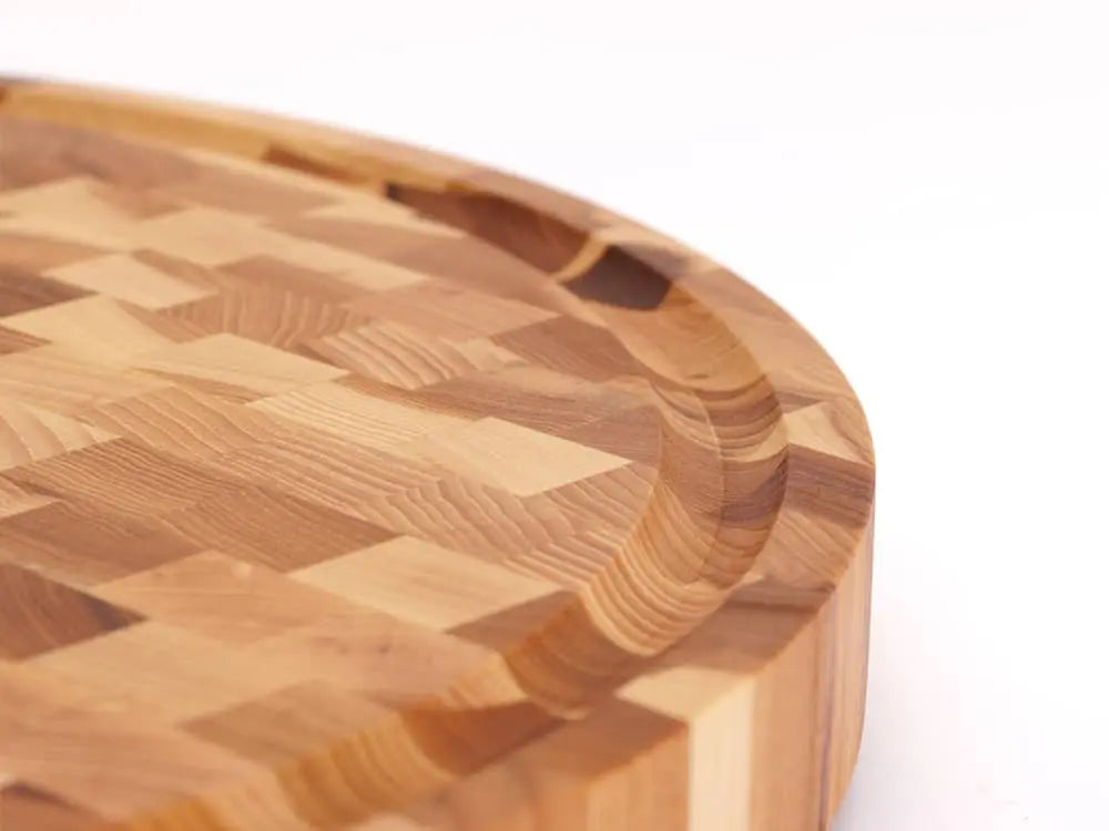A close-up, top view of a round end grain cutting board with a checkered pattern, with a focus on its unique juice groove