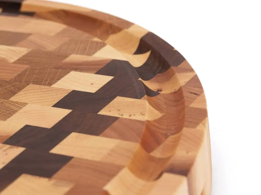 A close-up, top view of a round end grain cutting board with a checkered pattern, with a focus on its unique juice groove