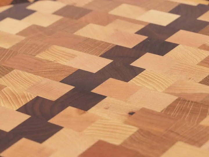 Close-up top view of a round end-grain cutting board with a checkered pattern of various wood tones, showing the intricate grain and texture