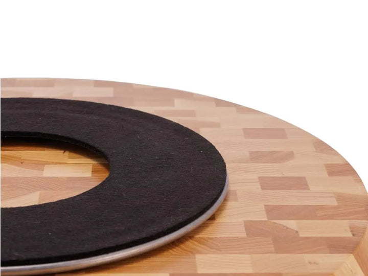 Close-up view of the underside of a round end-grain lazy susan with a light brown geometric mosaic pattern in hickory wood, showing a black protective felt pad, on a white background
