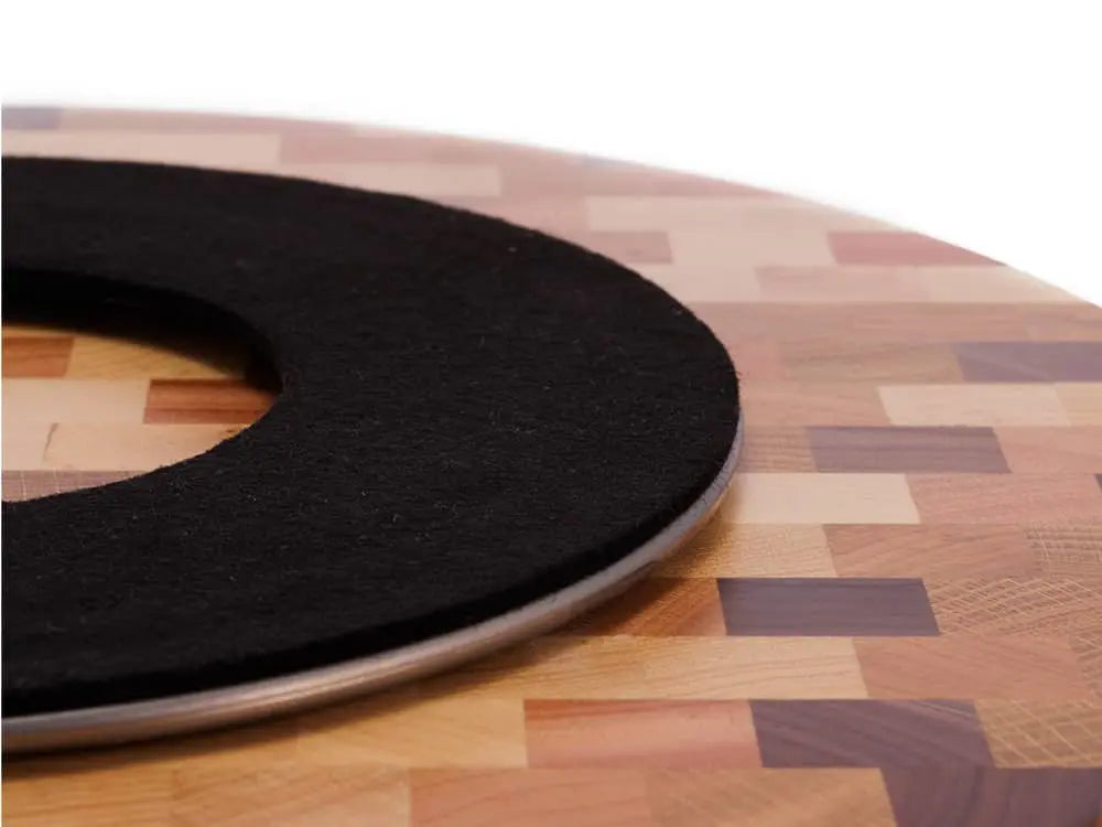 Bottom view of a round end-grain lazy susan with a geometric mosaic pattern in various shades of brown and beige wood, showing a black protective felt pad, on a white background