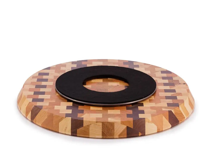Bottom view of a round end-grain lazy susan with a geometric mosaic pattern featuring dark brown vertical stripes and lighter brown squares, showing a black protective felt pad, on a white background