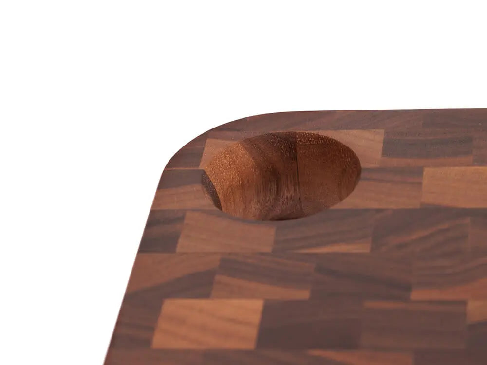 A close-up, top view of a black walnut end grain charcuterie board board with a checkered pattern, with a focus on its unique handle