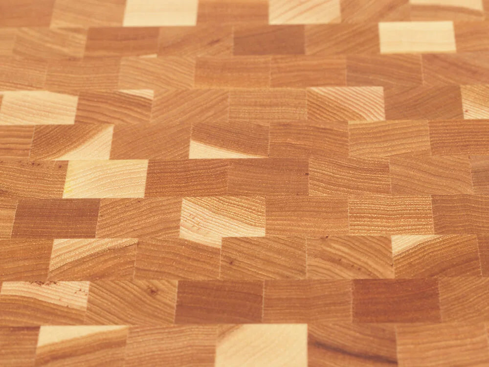 Close-up, top view of an end-grain charcuterie board with a checkered pattern of various wood tones, showing the intricate grain and texture