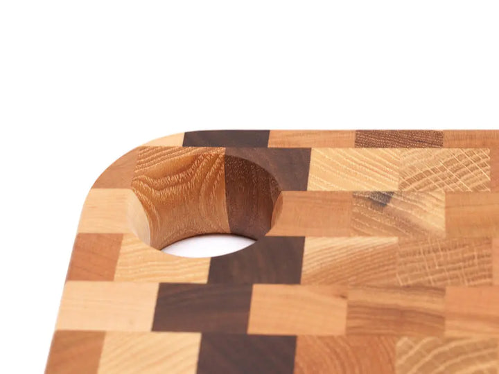 A close-up, top view of an end grain charcuterie board board with a checkered pattern, with a focus on its unique handle