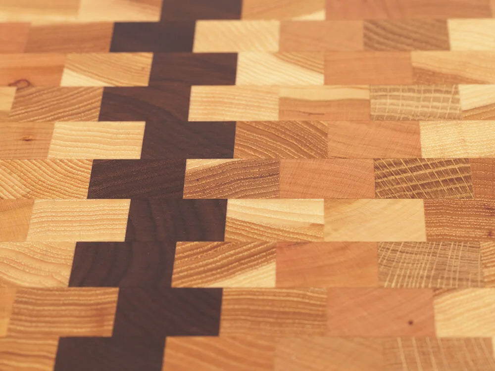 Close-up top view of an end-grain charcuterie board with a checkered pattern of various wood tones, showing the intricate grain and texture