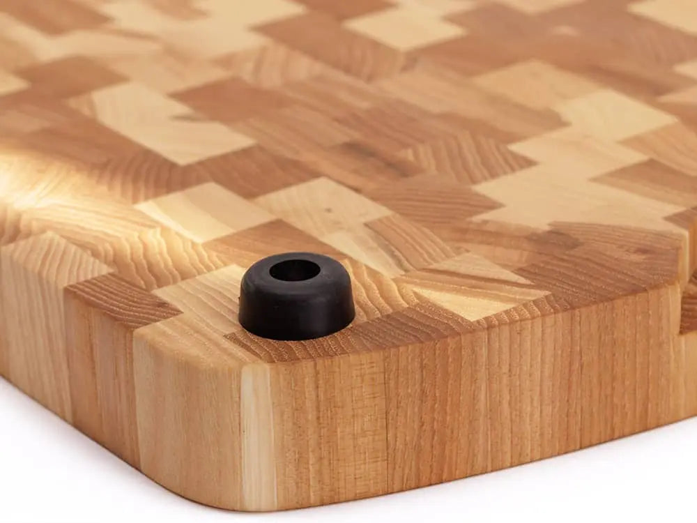Close-up of the bottom of a Hickory Nut end-grain cutting board with a checkered pattern and black rubber feet, against a white background