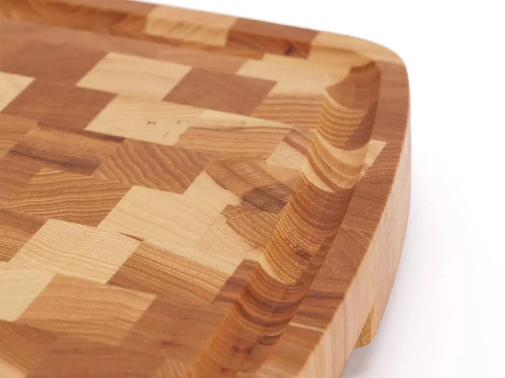 A close-up, top view of a Hickory Nut end grain cutting board with a checkered pattern and rounded edges, with a focus on the juice groove