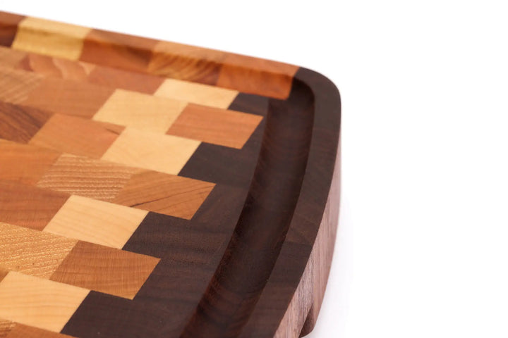 A close-up, top view of an end grain cutting board with a checkered pattern and rounded edges, with a focus on the juice groove