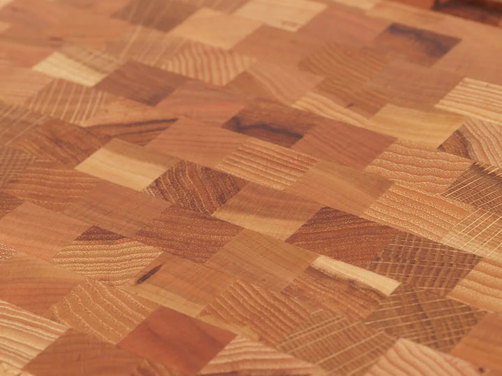 Close-up view of an end-grain cutting board with a checkered pattern of various wood tones, showing the intricate grain and texture
