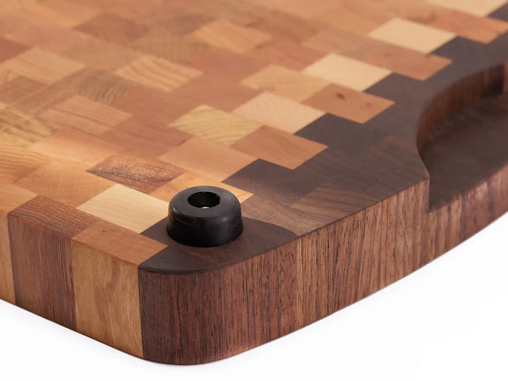 Close-up view of the bottom of an end-grain cutting board with a checkered pattern and black rubber feet, against a white background