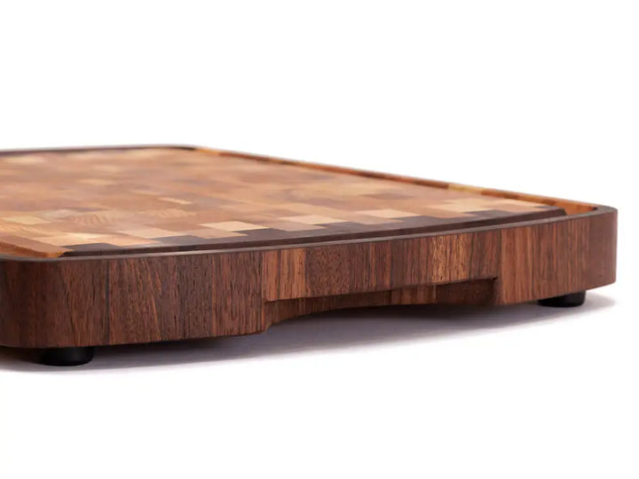 Side view of an end-grain cutting board with a checkered pattern of various wood tones, featuring rounded corners and a smooth finish, against a white background